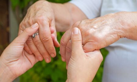 Zwei Hände, eine jüngere und eine ältere, halten sich sanft. Diese Geste symbolisiert Pflege und Unterstützung zwischen den Generationen