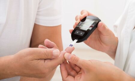 Ein Gesundheitsdienstleister führt einen Blutzuckertest durch, indem er einem Patienten einen Teststreifen in den Finger einführt. Diese Szene illustriert wichtige Aspekte der Diabetesüberwachung im Rahmen eines Pflegeratgebers