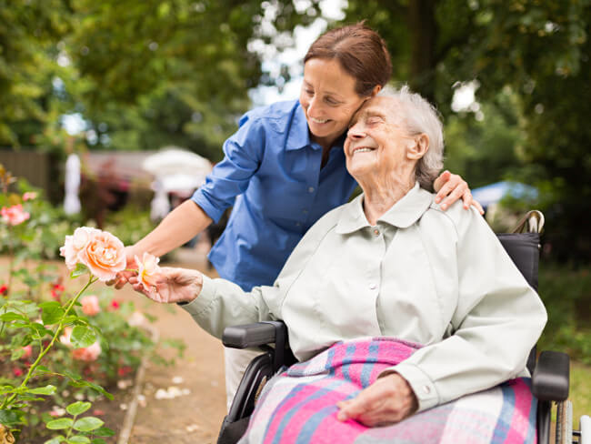 Betagte Seniorin im Rollstuhl wird von einer Pflegekraft liebevoll umarmt